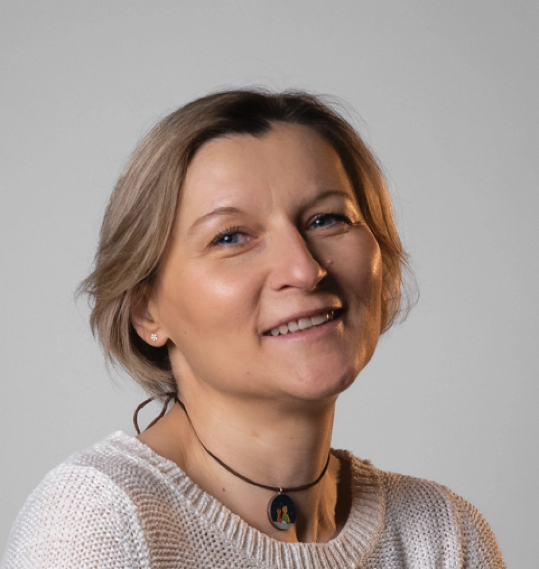 Uśmiechnięta kobieta w swetrze, z krótkimi włosami i naszyjnikiem. Tło jasne.