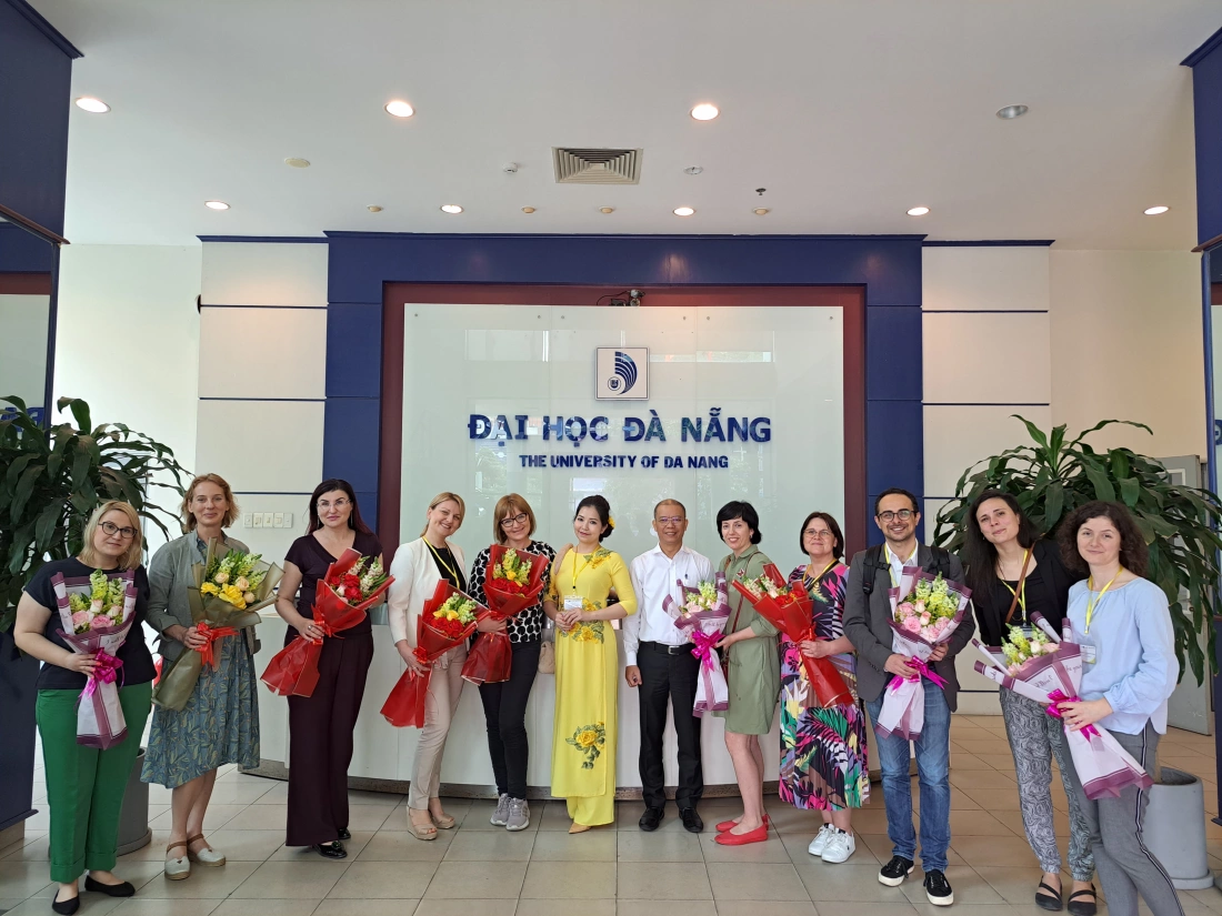 Grupa ludzi trzymająca bukiety kwiatów stoi przed budynkiem uniwersytetu w Da Nang.