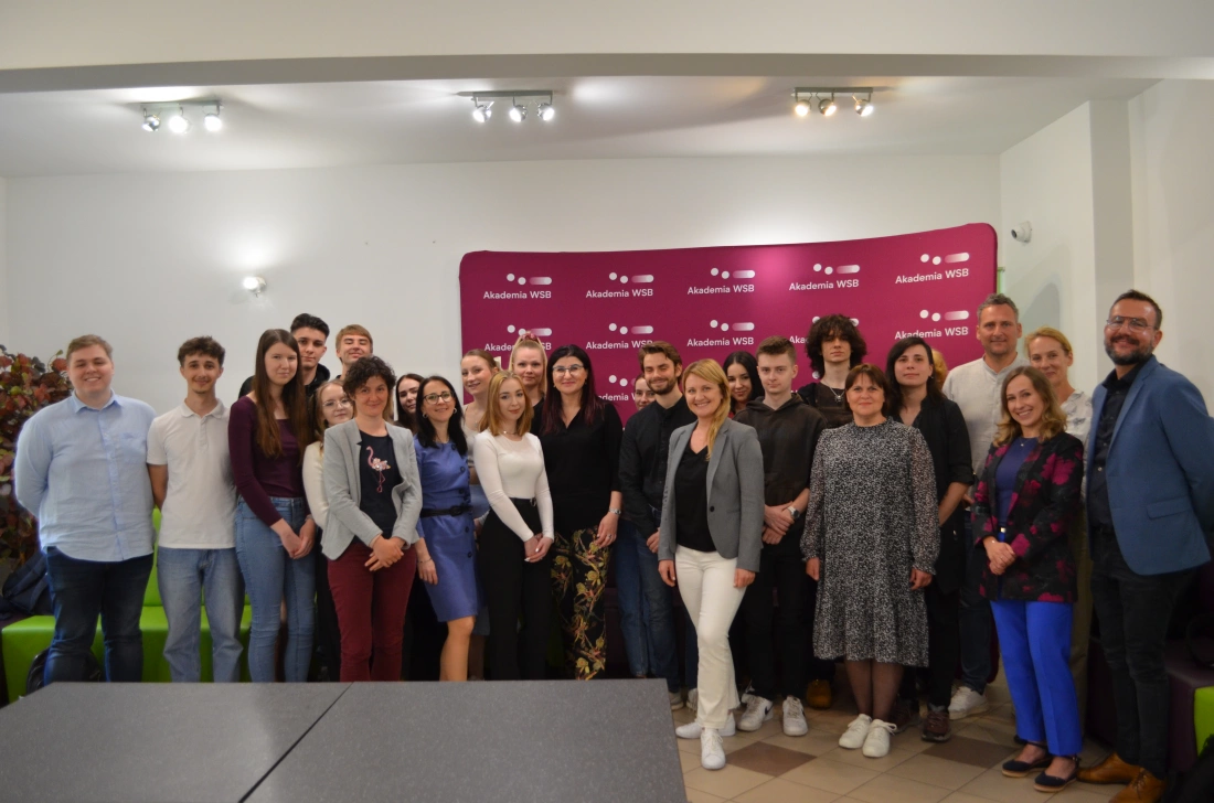 Grupa ludzi pozujących do zdjęcia przed tłem z logo Akademii WSB.