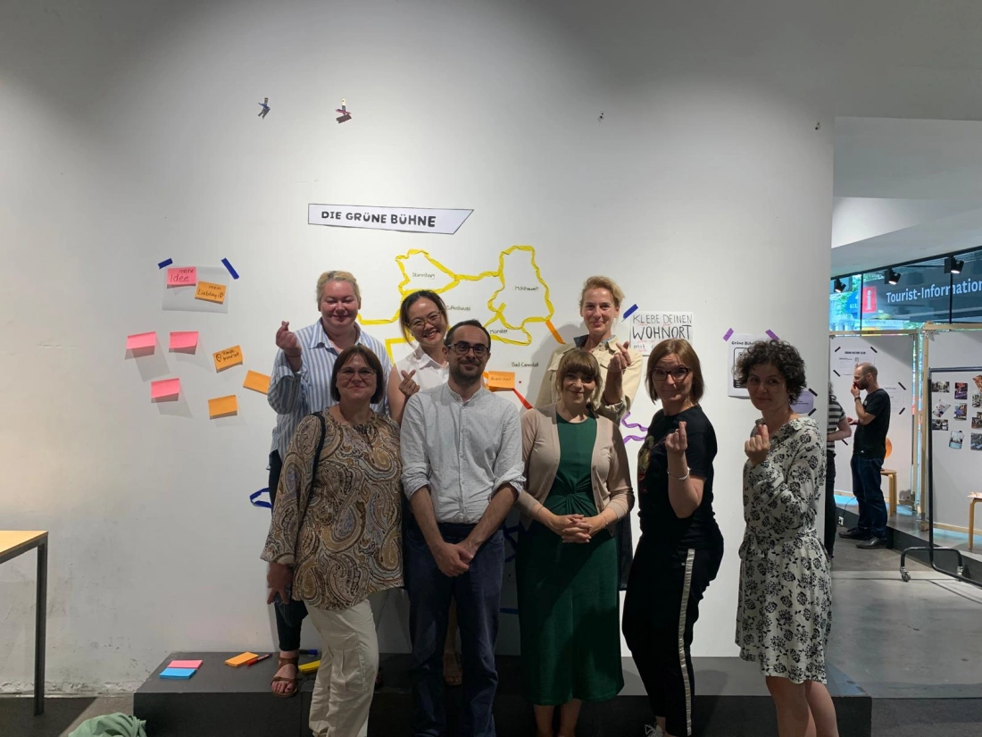 Grupa ludzi pozujących razem przed ścianą z graficznymi elementami i kolorowymi notatkami.