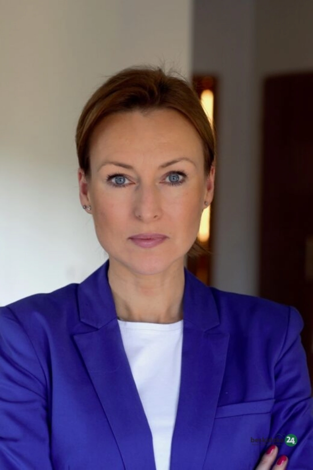 Kobieta w niebieskiej marynarce, z zamkniętymi ramionami i poważnym wyrazem twarzy.