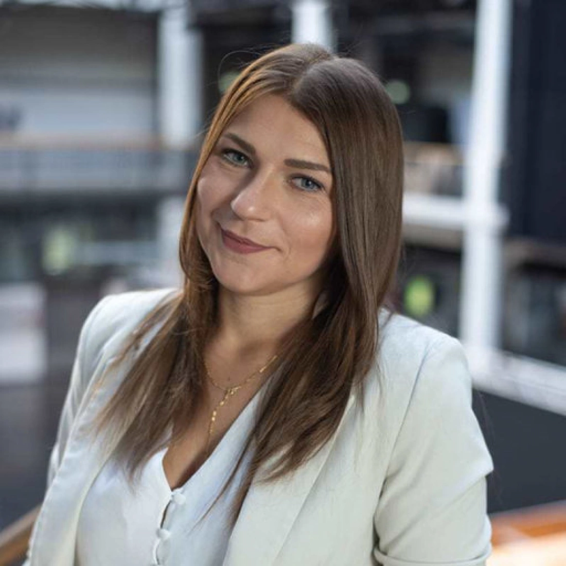 Młoda kobieta w jasnym ubraniu, uśmiechająca się na tle nowoczesnego wnętrza.