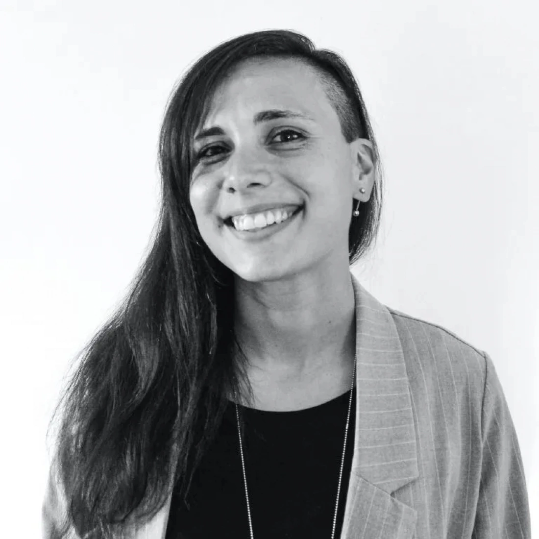 Kobieta z długimi, ciemnymi włosami i uśmiechem, ubrana w marynarkę, na jasnym tle.