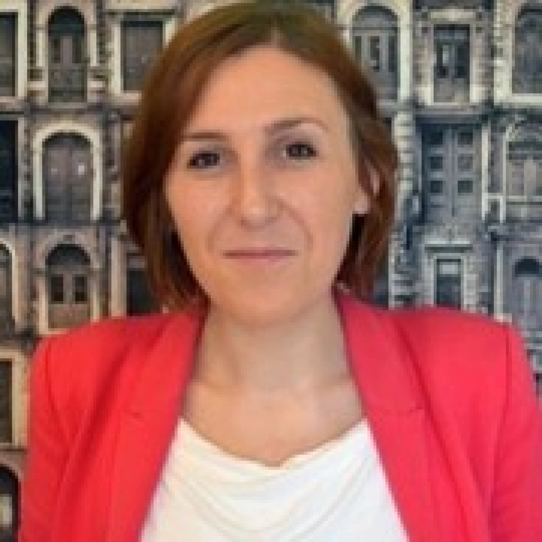 Kobieta w różowej marynarce na tle budynków.