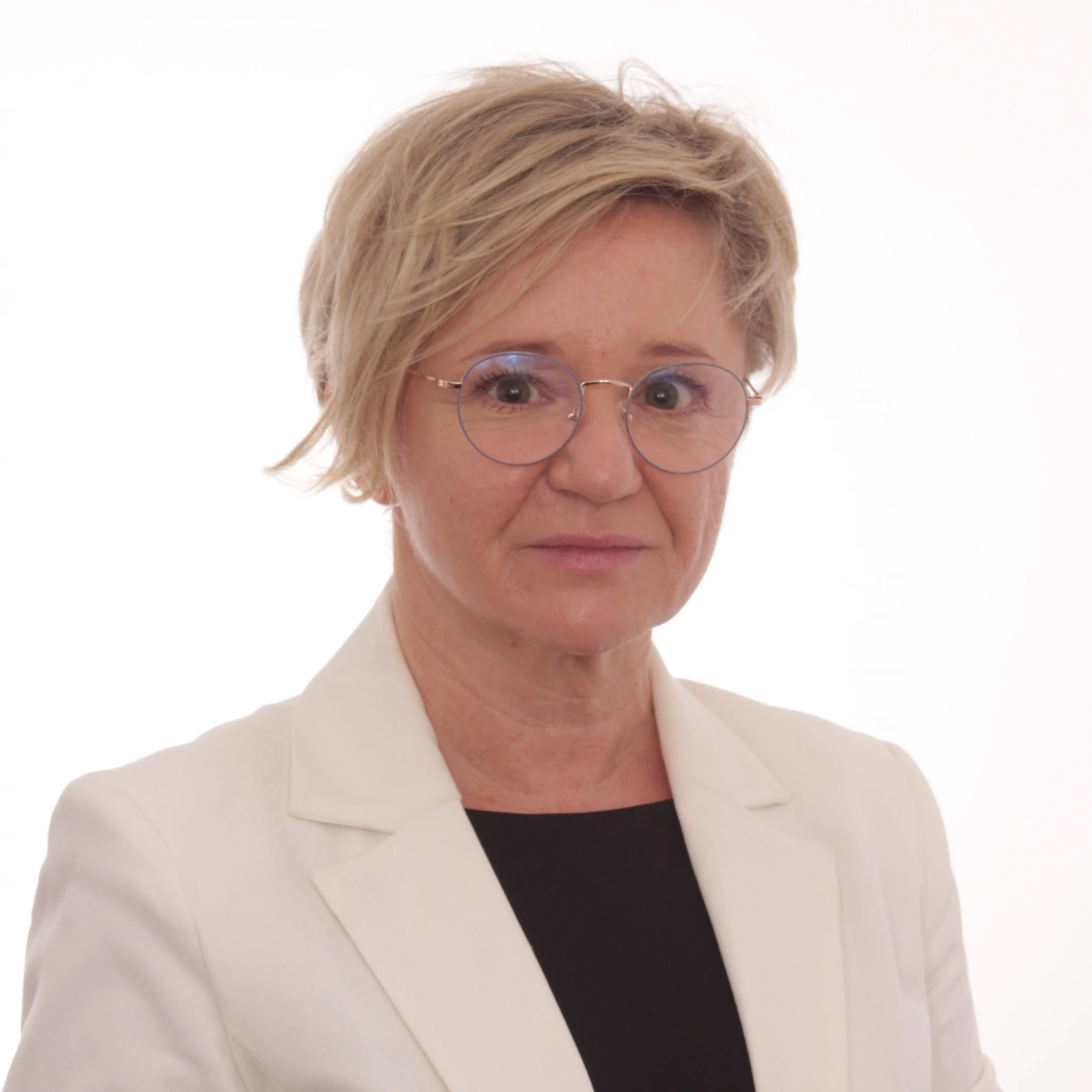 Kobieta w białym garniturze, z krótkimi włosami i okularami, na neutralnym tle.