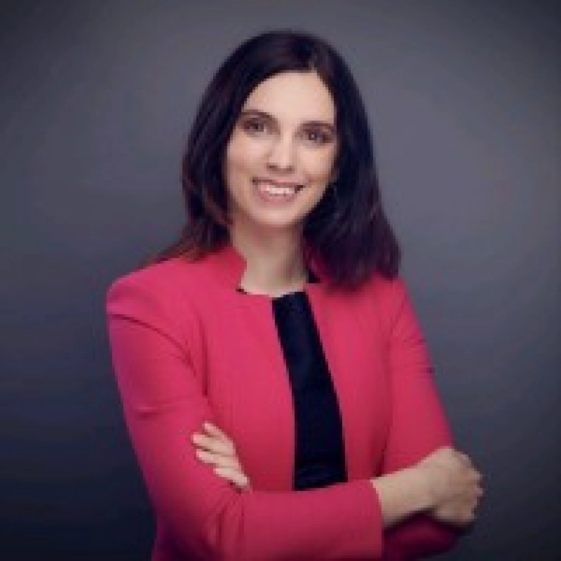 Kobieta w różowej marynarce uśmiecha się, mając za sobą ciemne tło.