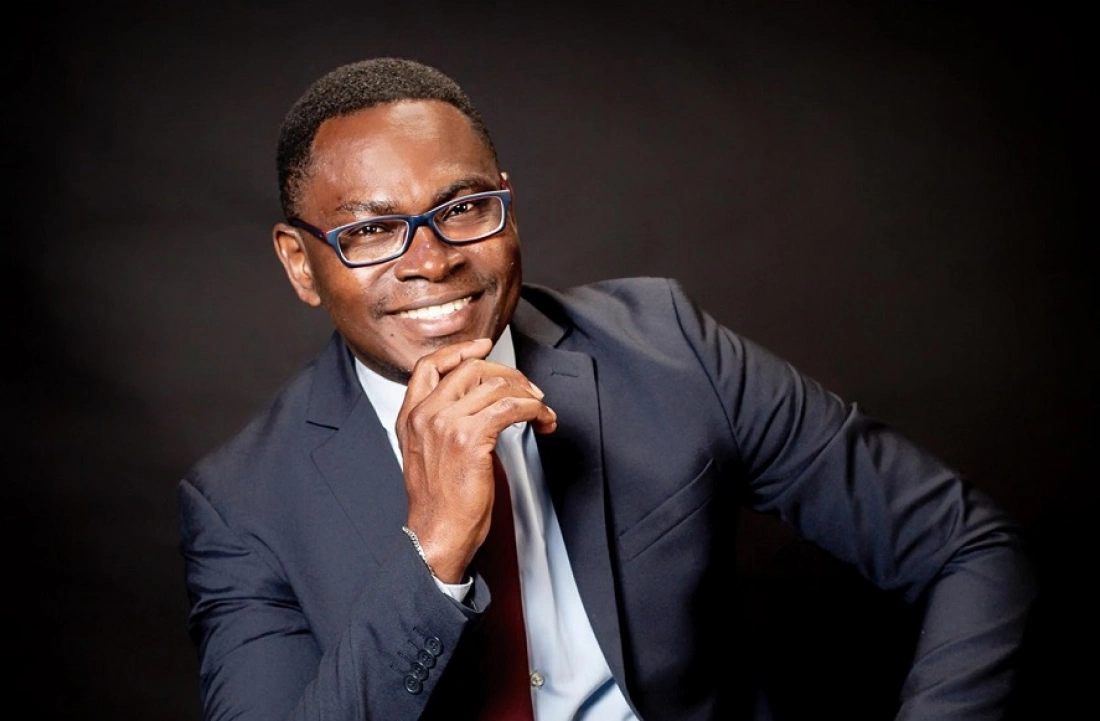 Mężczyzna w garniturze z uśmiechem, trzymając rękę przy brodzie.