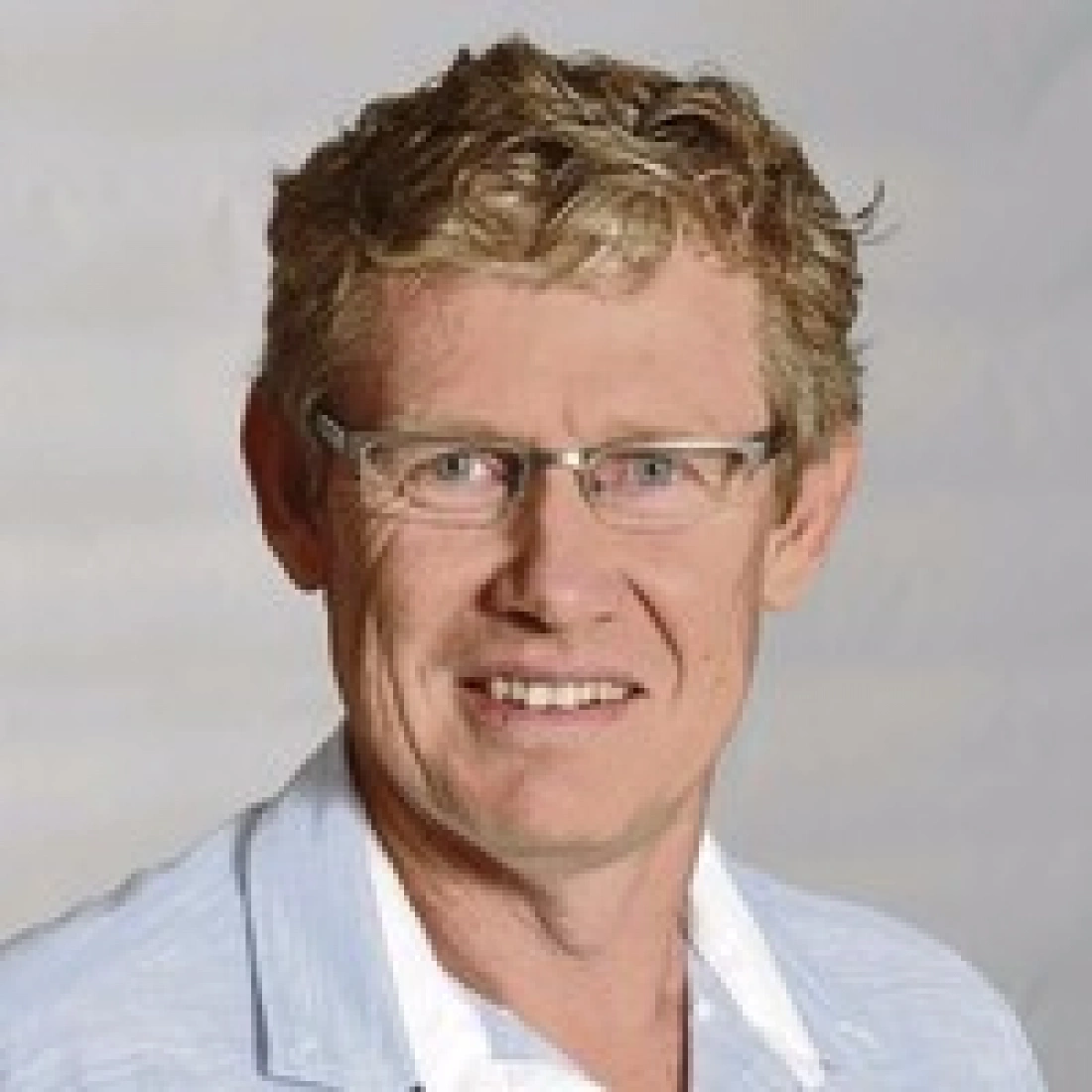 Mężczyzna z kręconymi włosami, w okularach, uśmiechający się do kamery.