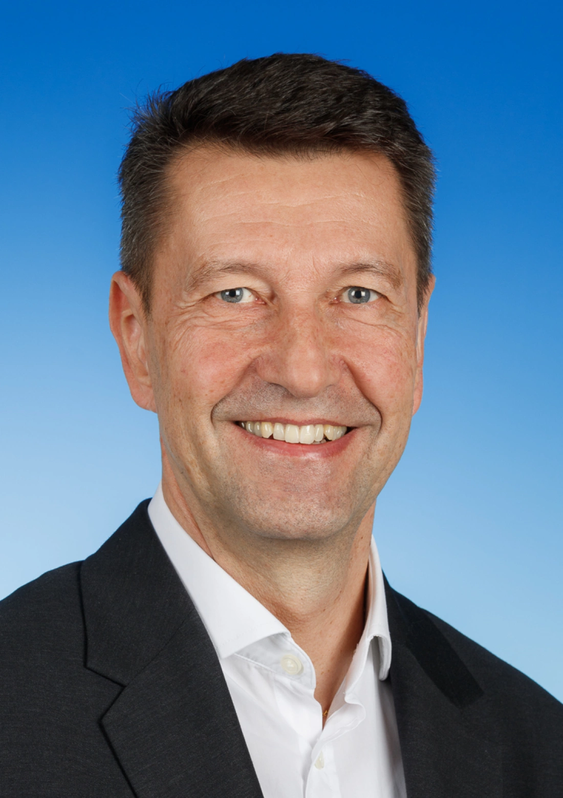 Mężczyzna w garniturze uśmiecha się na tle niebieskiego tła.