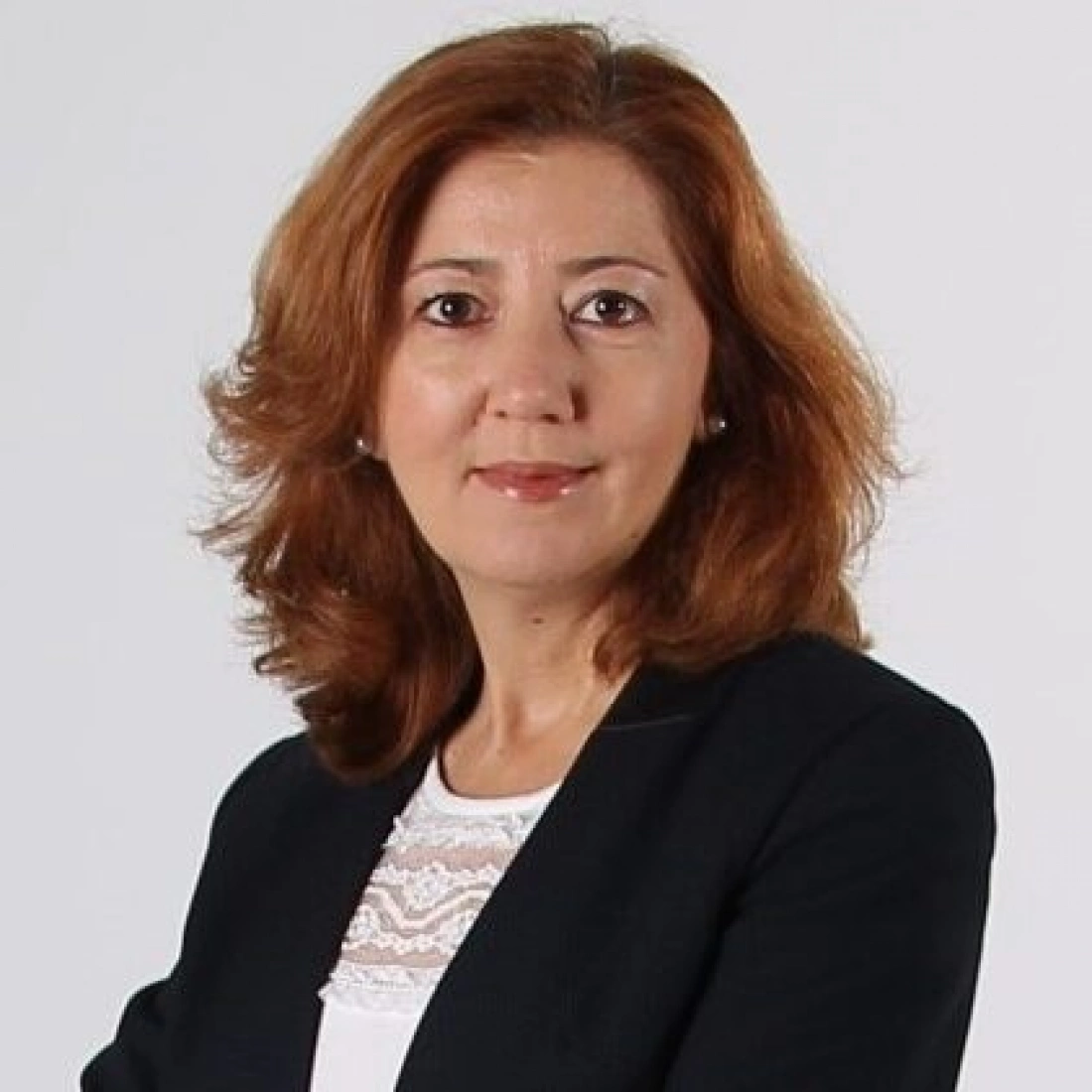 Kobieta z brązowymi włosami, w czarnym żakiecie, stoi na jasnym tle.