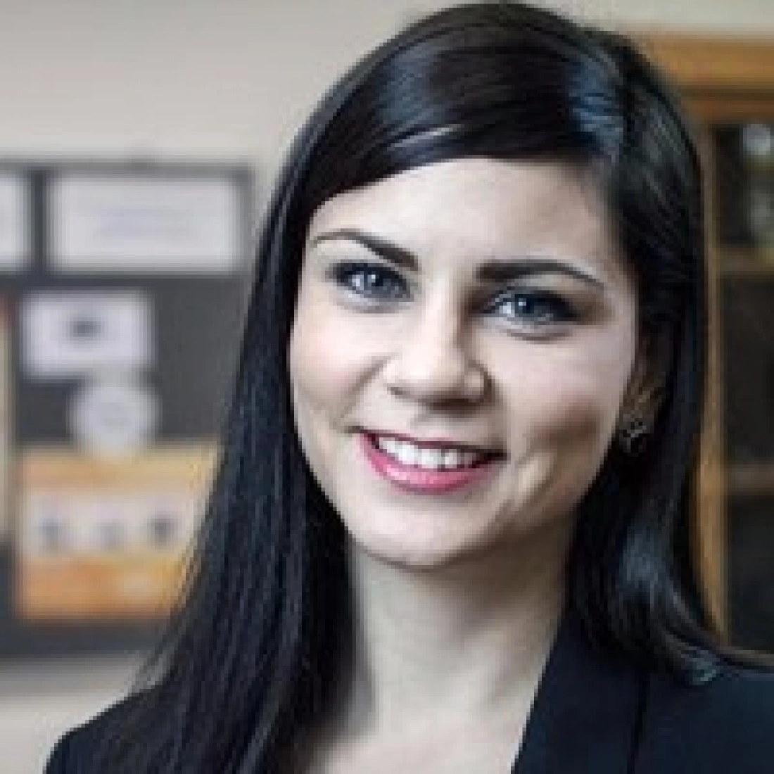 Kobieta z długimi, ciemnymi włosami, uśmiechająca się, w eleganckim ubraniu.