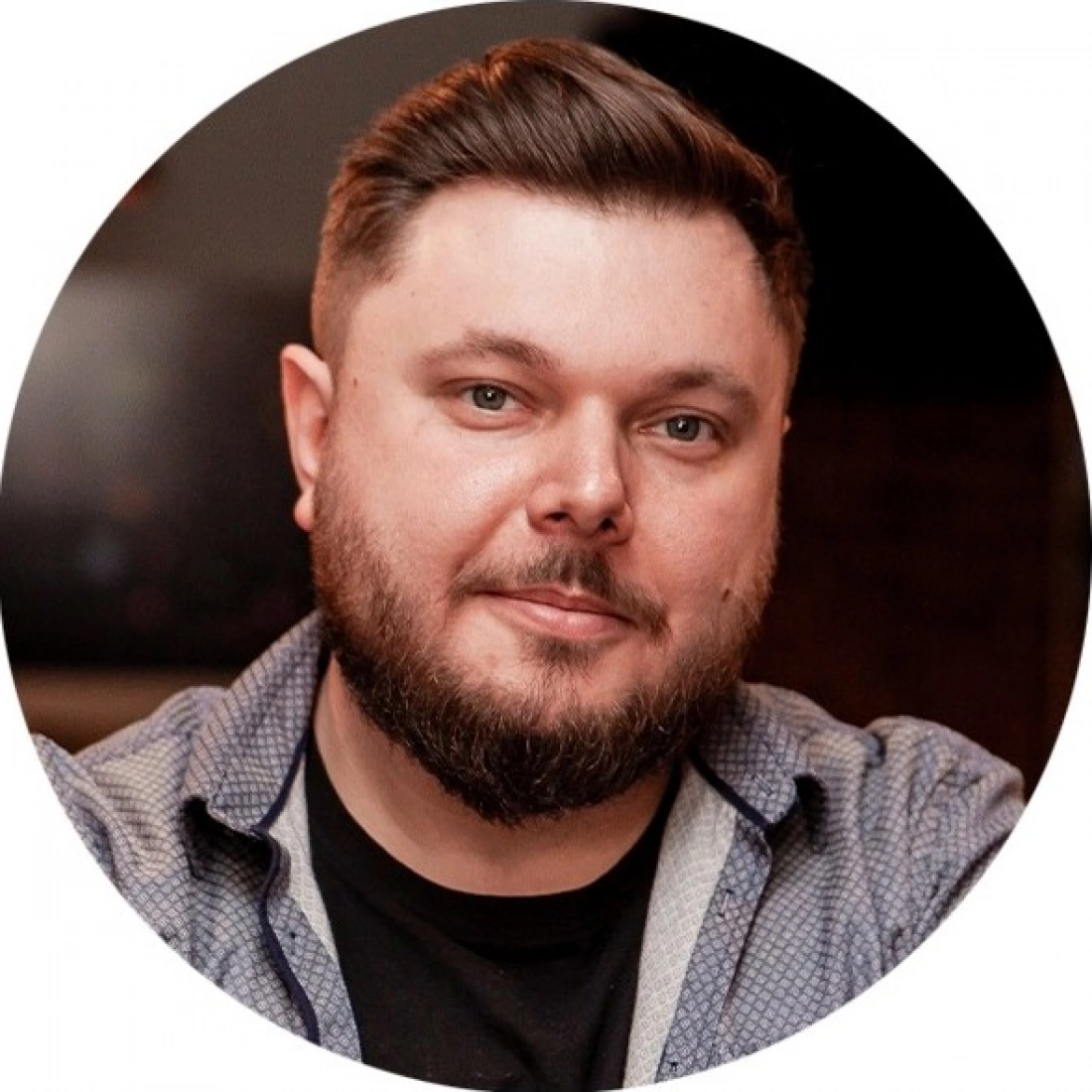 Mężczyzna z brodą i krótkimi, ciemnymi włosami, uśmiechający się w okrągłej ramce.