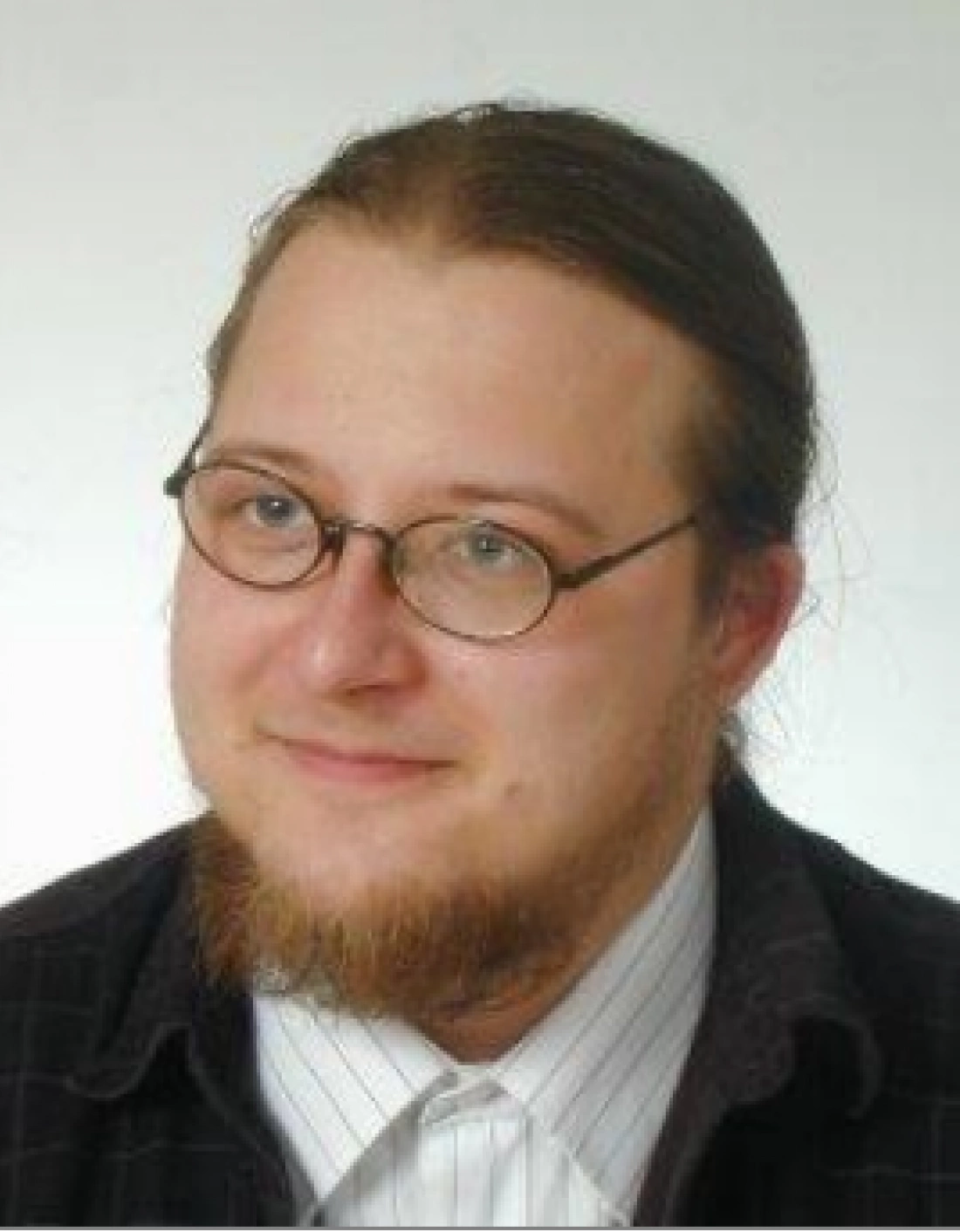 Mężczyzna z okularami, uśmiechający się na tle jasnego tła.