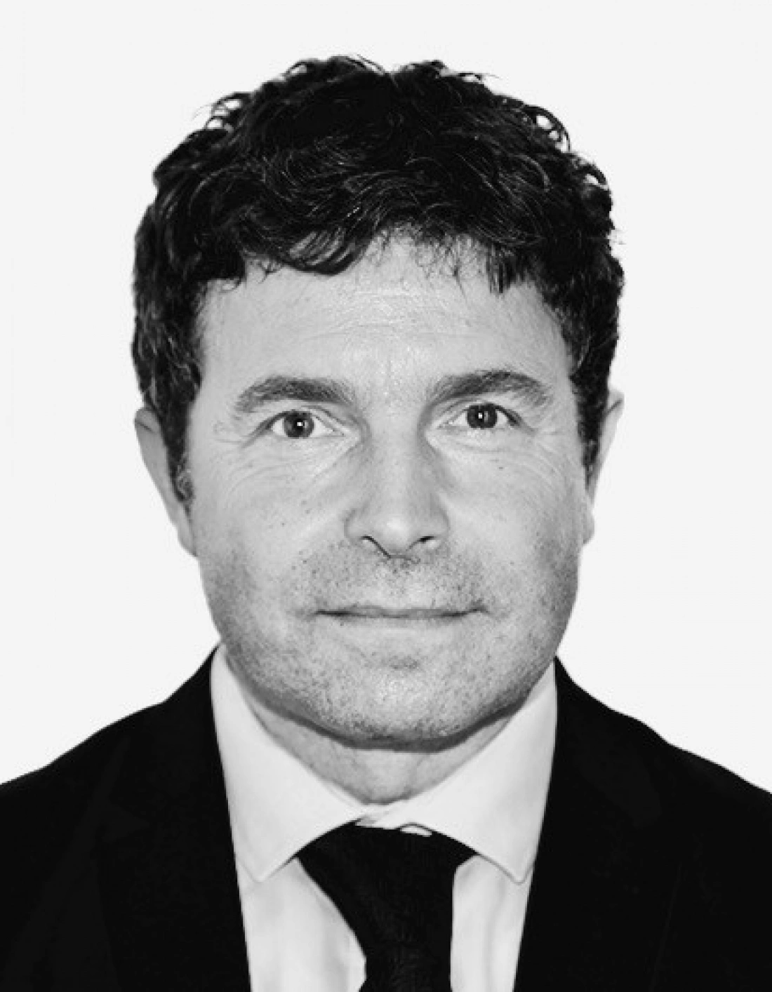 Mężczyzna w eleganckim garniturze, z uśmiechem, na jasnym tle.