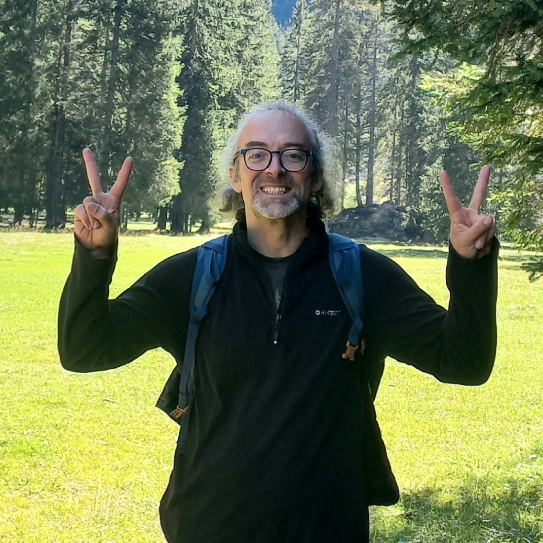 Uśmiechający się mężczyzna w parku, robiący znak pokoju w obie ręce.