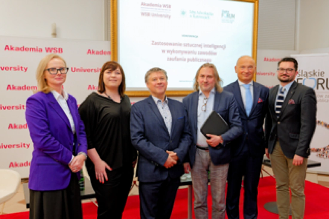 Zespół ludzi stojących przy stoisku, w tle banery Akademii WSB oraz prezentacja na temat strategii inteligentnego wykorzystania zaufania publicznego.