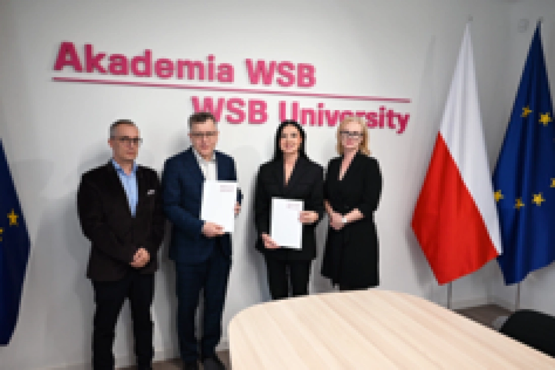 Cztery osoby stoją przy stole, trzymając dokumenty, w tle logo Akademii WSB oraz flagi Polski i Unii Europejskiej.