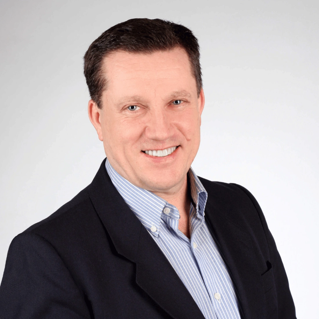 Mężczyzna w garniturze, uśmiechający się na tle szaro-białym.