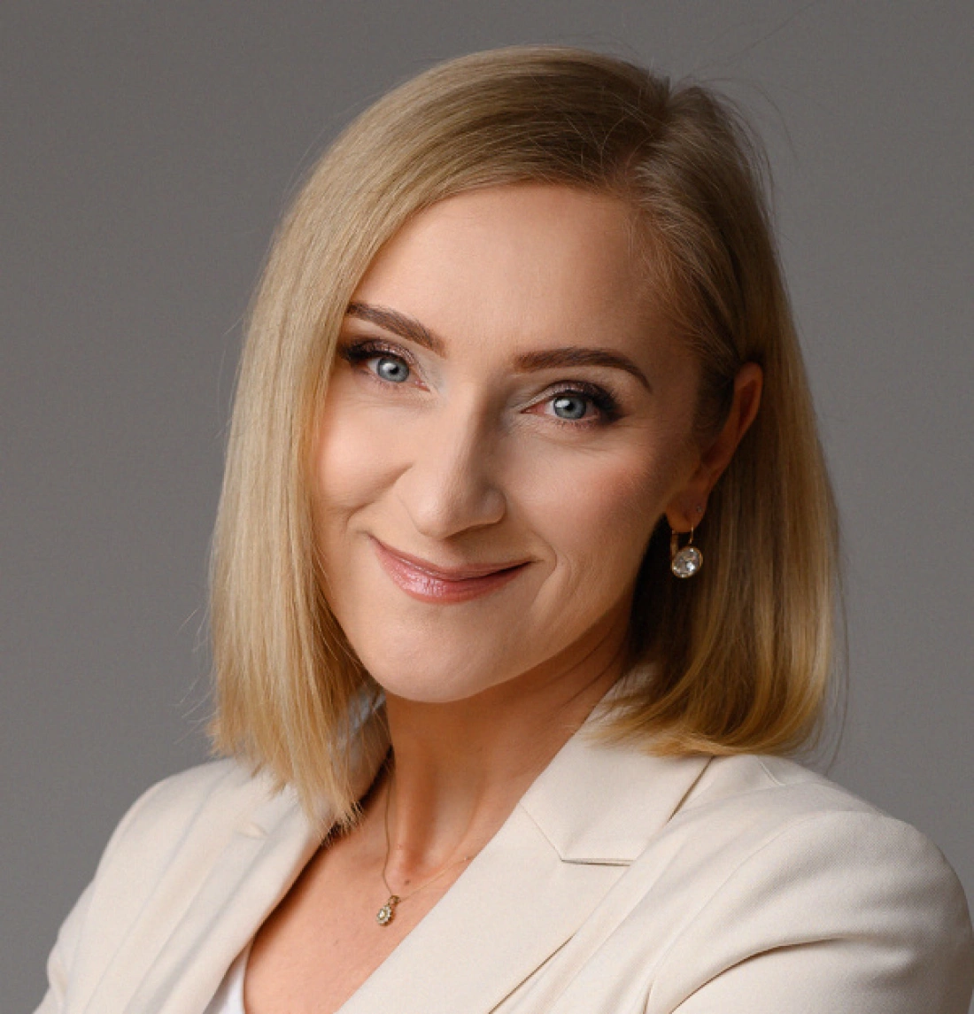 Kobieta z krótkimi, blond włosami, uśmiechająca się w eleganckim ubraniu.