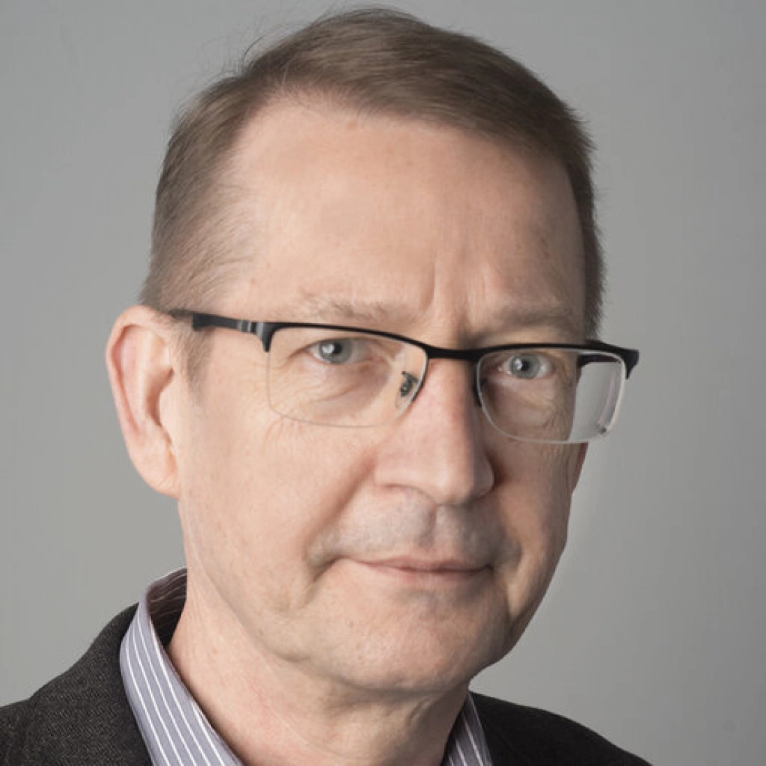 Mężczyzna w okularach, z delikatnym uśmiechem, ubrany w elegancką koszulę.