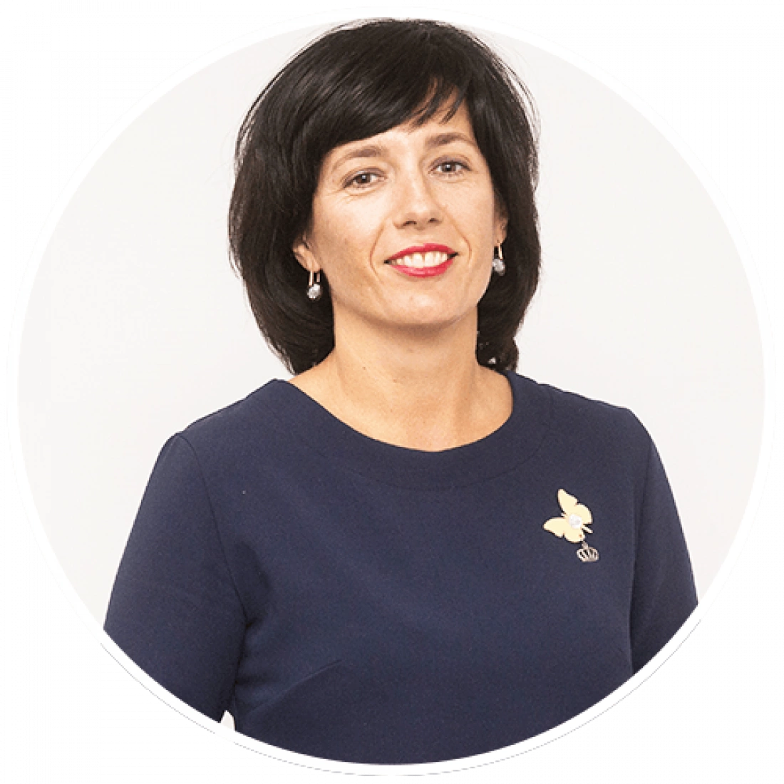 Kobieta w granatowej bluzce z delikatnym uśmiechem, nosząca biżuterię oraz ozdobę w kształcie motyla.