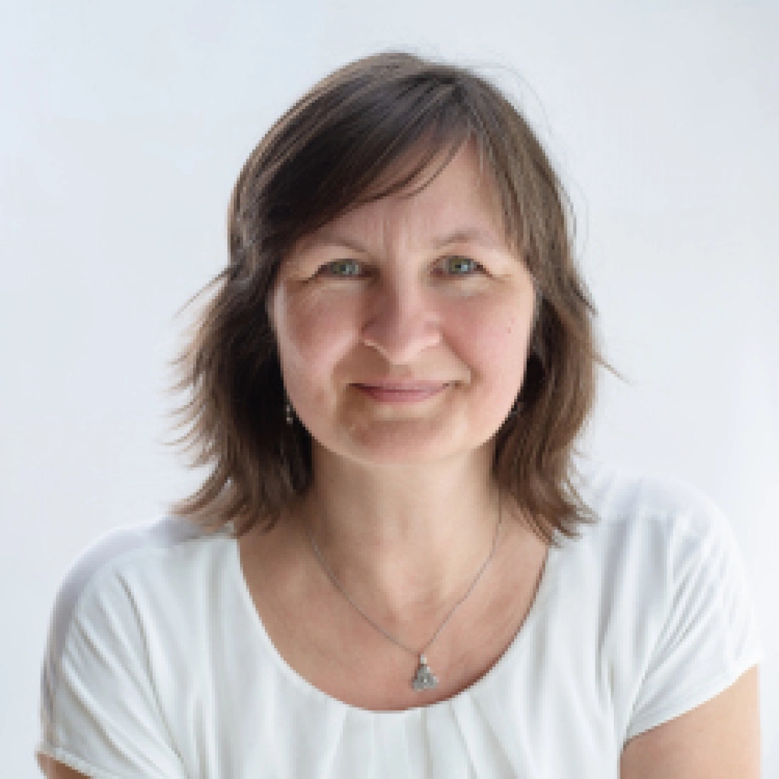 Portret kobiety z uśmiechem, w białej bluzce na tle jasnego tła.