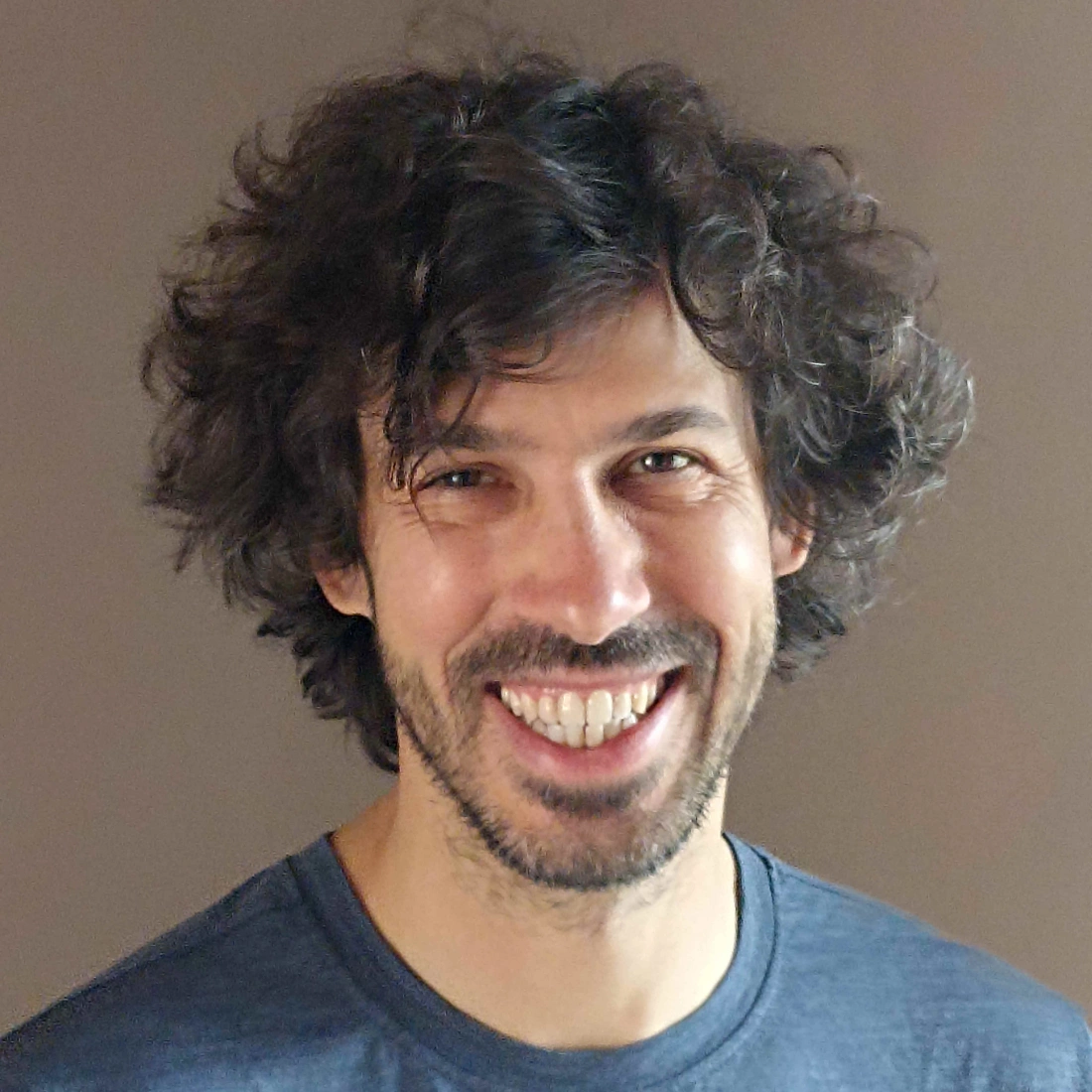 Mężczyzna z kręconymi włosami uśmiecha się.