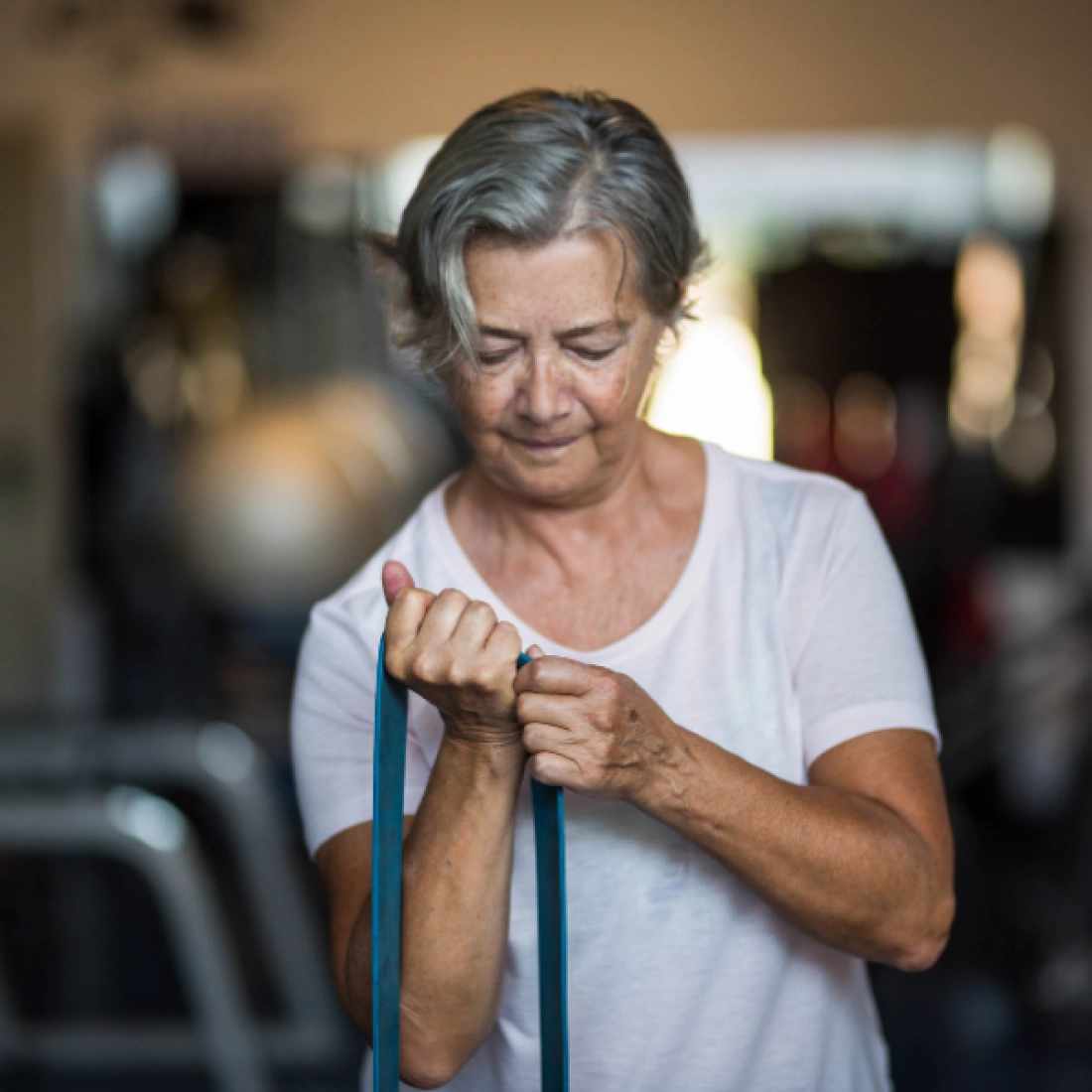 Starsza kobieta ćwiczy z gumą oporową w siłowni.