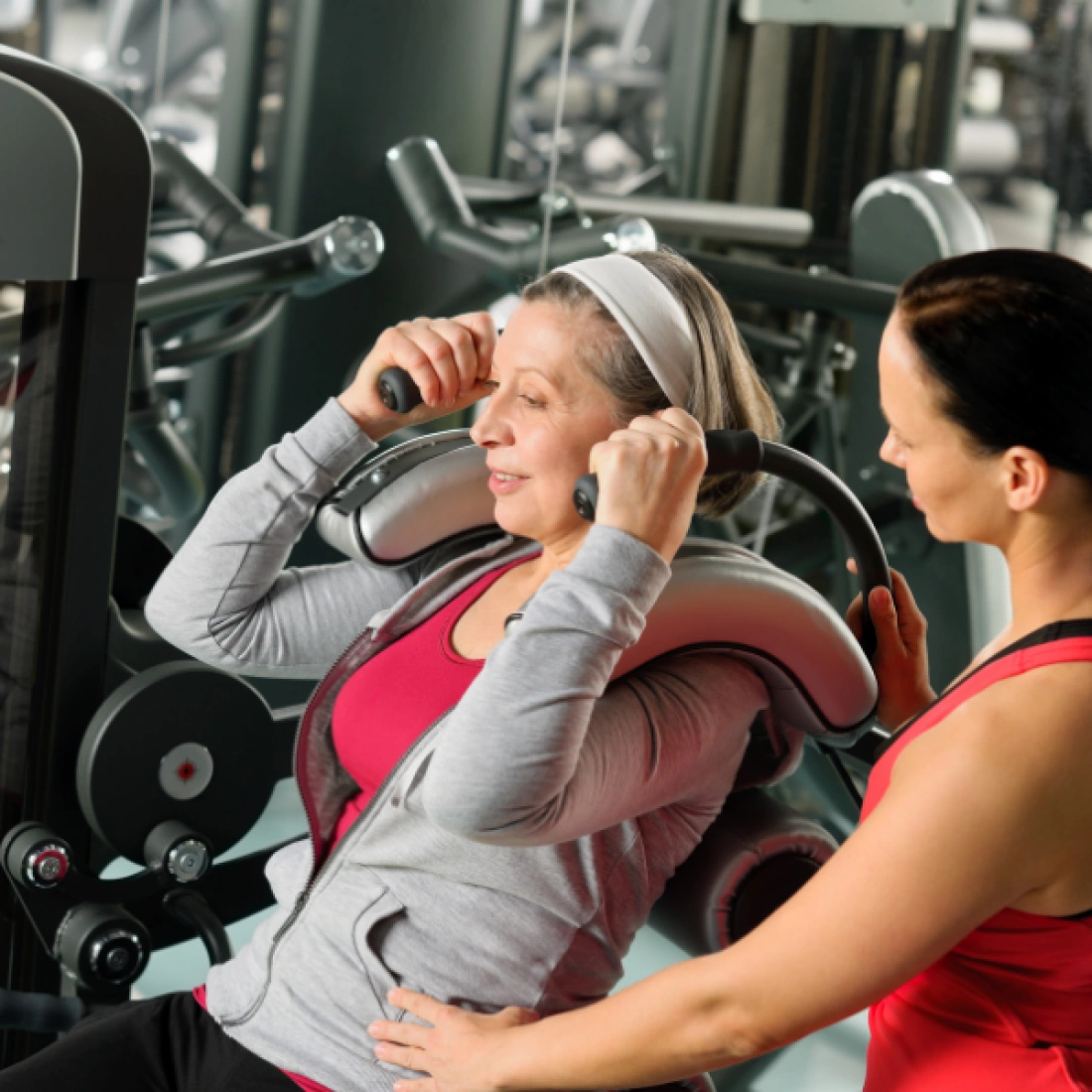 Kobieta ćwiczy na maszynie w siłowni z pomocą instruktorki.
