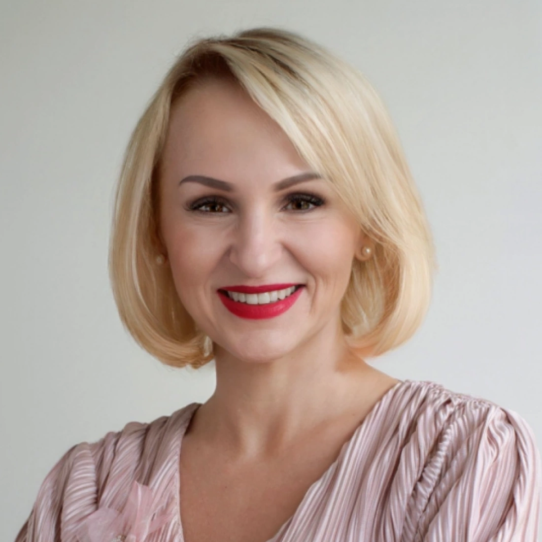 Uśmiechnięta kobieta z krótkimi, blond włosami, ubrana w różową bluzkę.