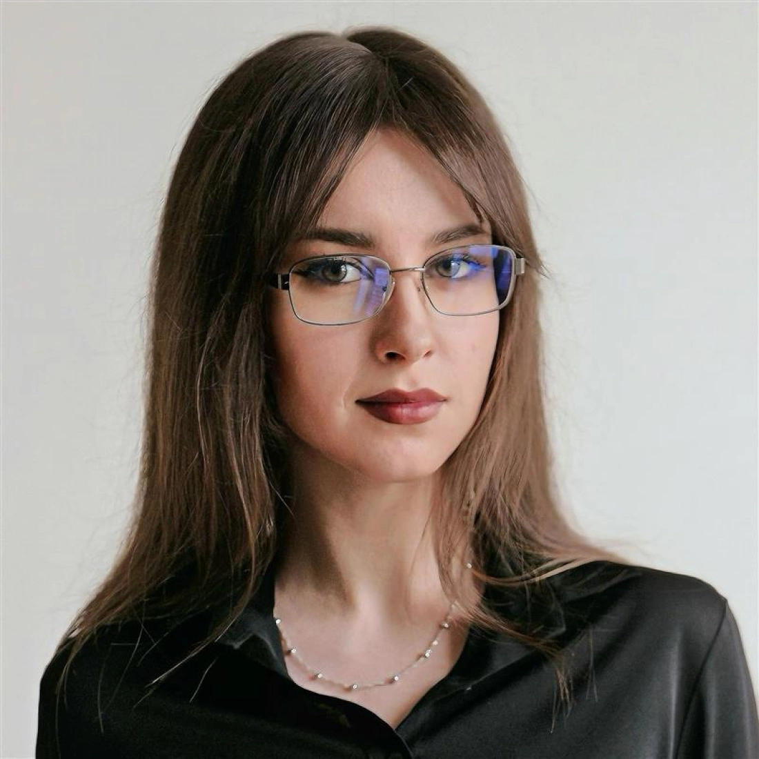 Młoda kobieta z długimi włosami, w okularach, ubrana w czarną koszulę i naszyjnik.