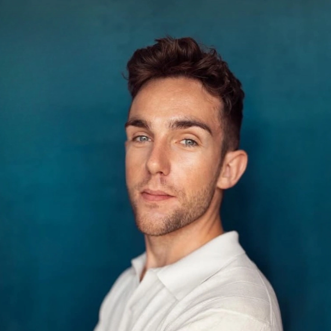 Mężczyzna w jasnej koszuli z lekkim uśmiechem, stojący na tle w odcieniach niebieskiego.