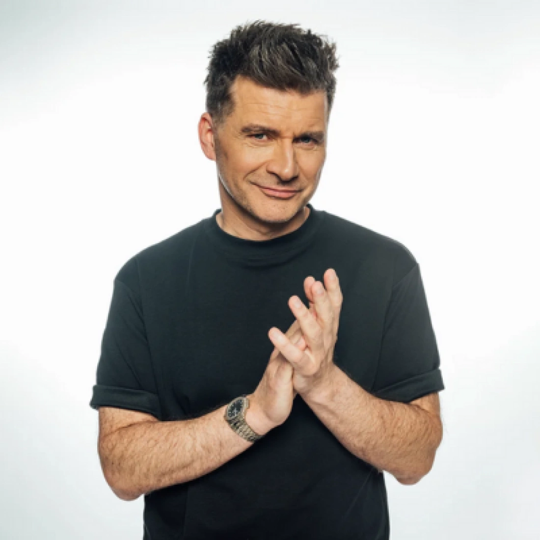 Mężczyzna w czarnej koszulce, uśmiechający się i klaskający w dłonie.