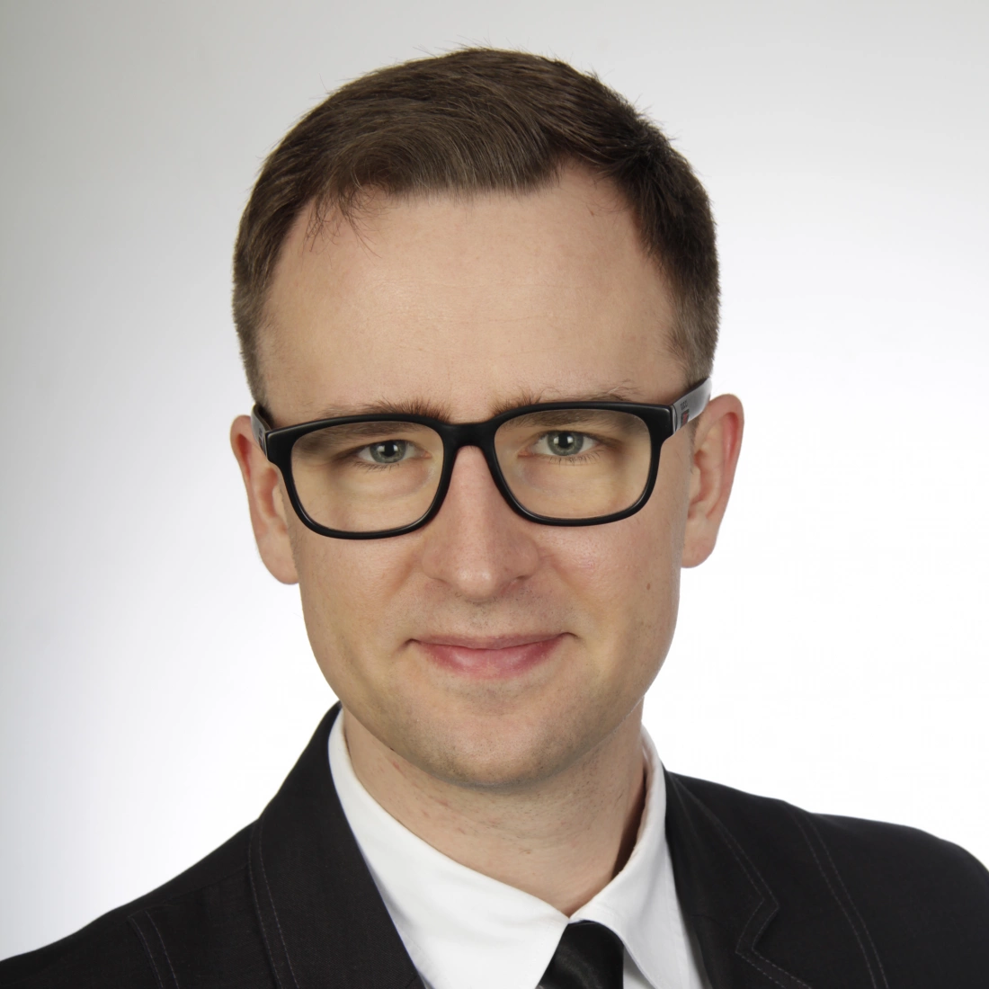 Mężczyzna w okularach, uśmiechający się, ubrany w elegancki garnitur.