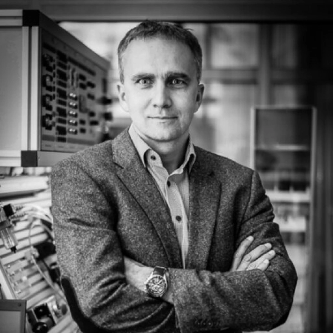 Mężczyzna w szarym garniturze stoi z założonymi rękami w nowoczesnym otoczeniu.