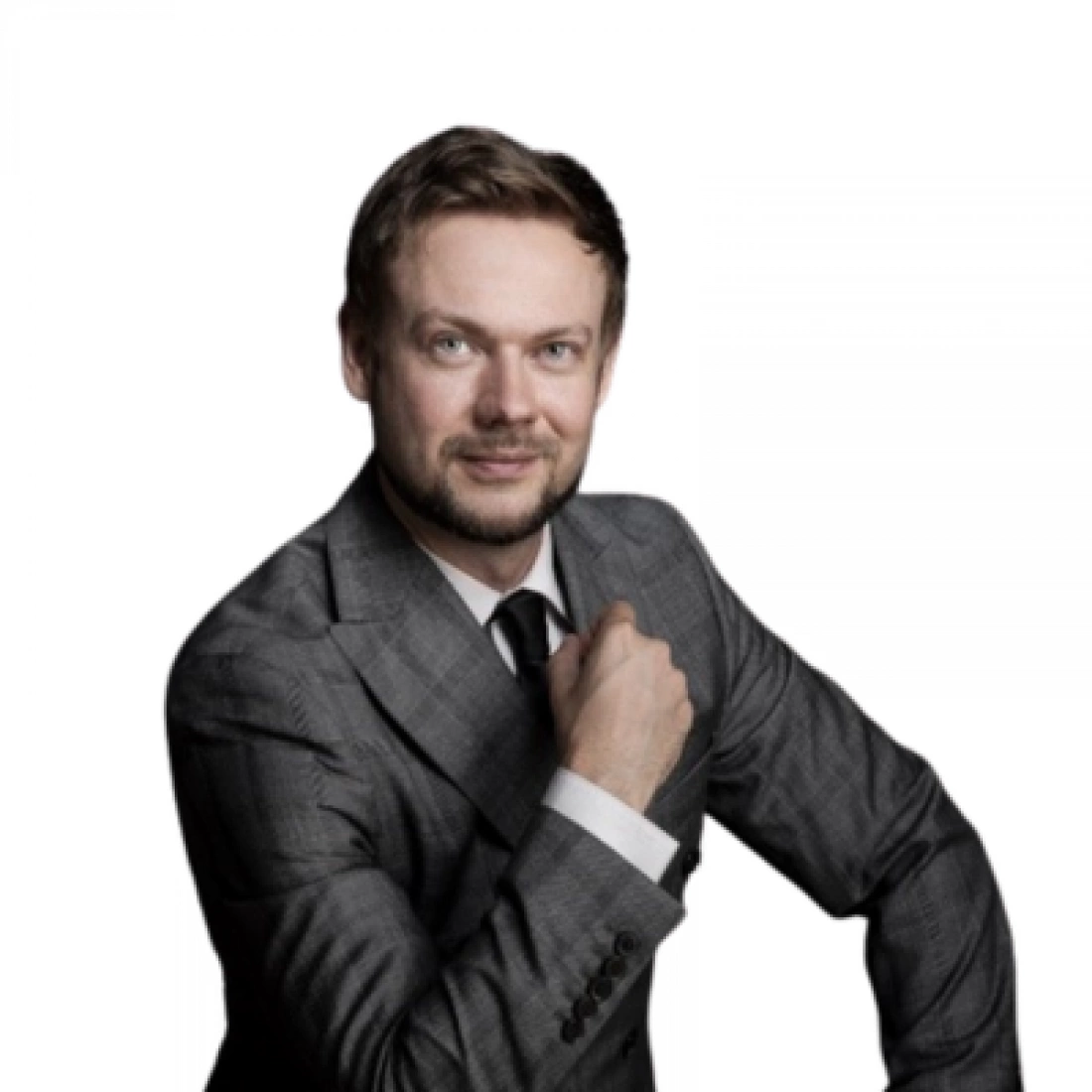 Mężczyzna w szarym garniturze z uśmiechem, trzymający dłoń na ramieniu.