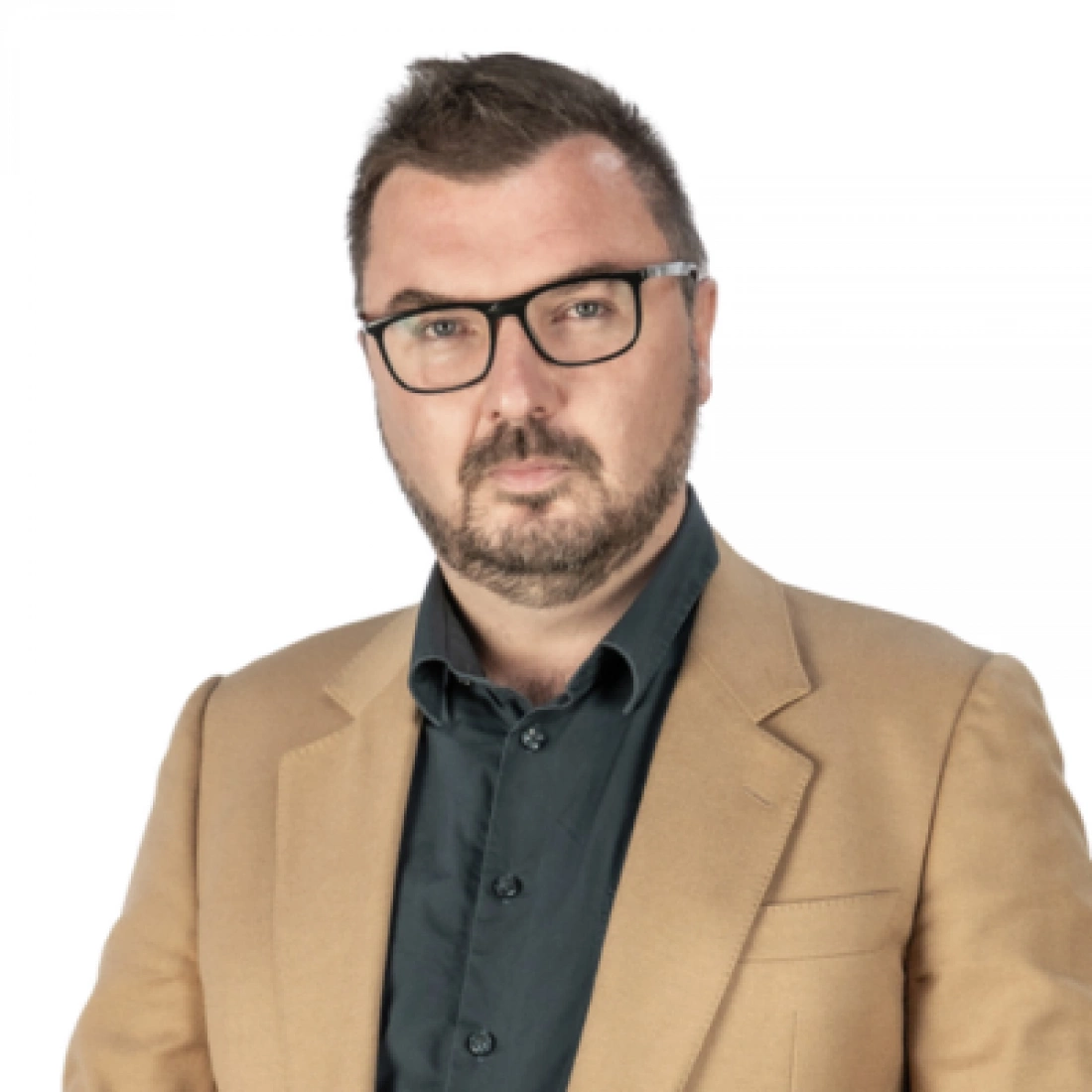 Mężczyzna w okularach, ubrany w beżowy żakiet, z poważnym wyrazem twarzy.