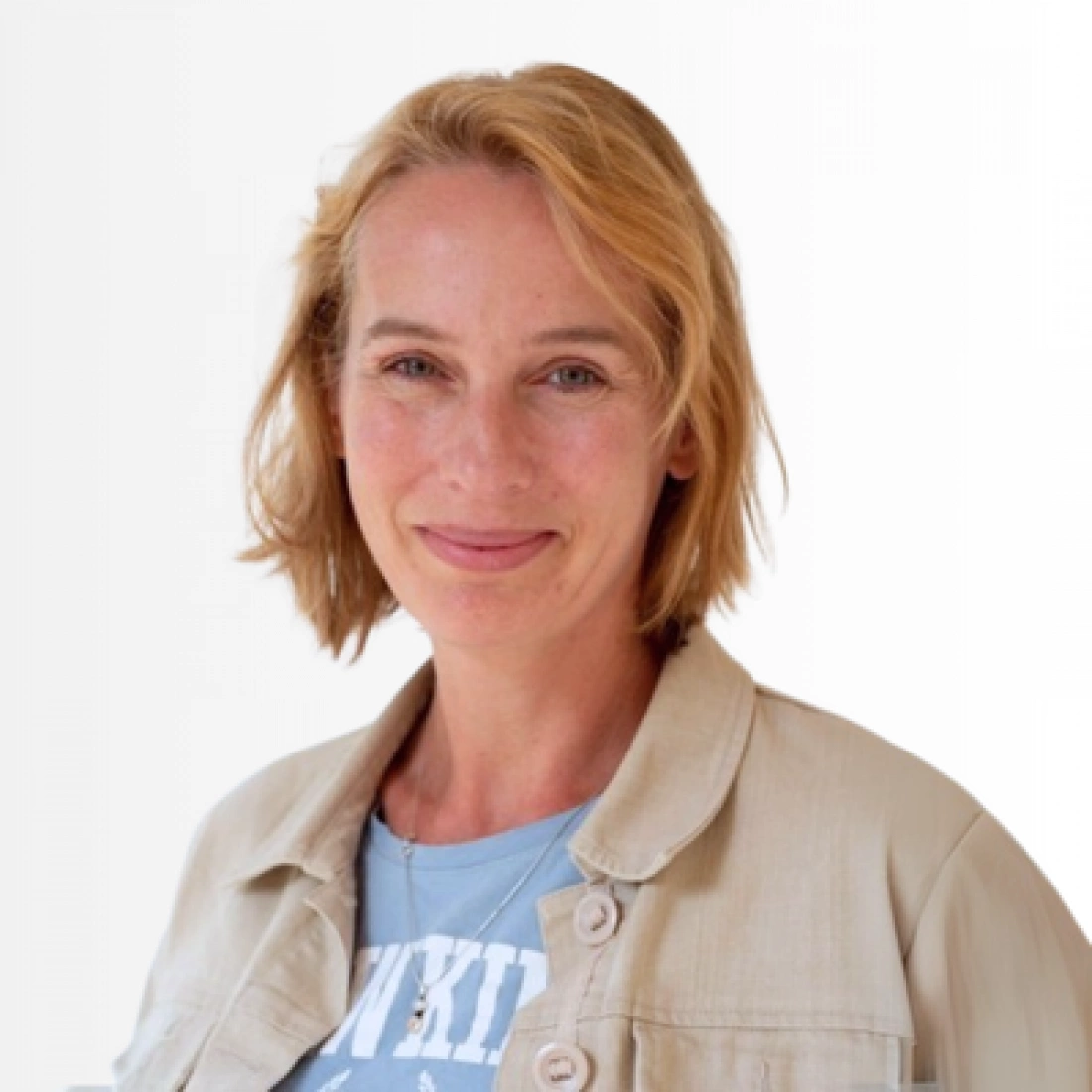 Kobieta z krótkimi, blond włosami, uśmiechająca się. Ubrana w jasną kurtkę i t-shirt.