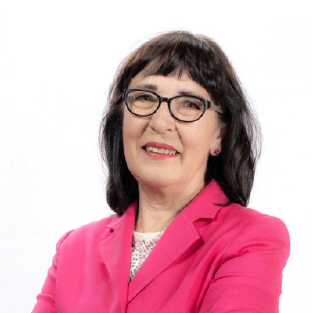 Kobieta w różowej marynarce, z okularami, uśmiechająca się do kamery.