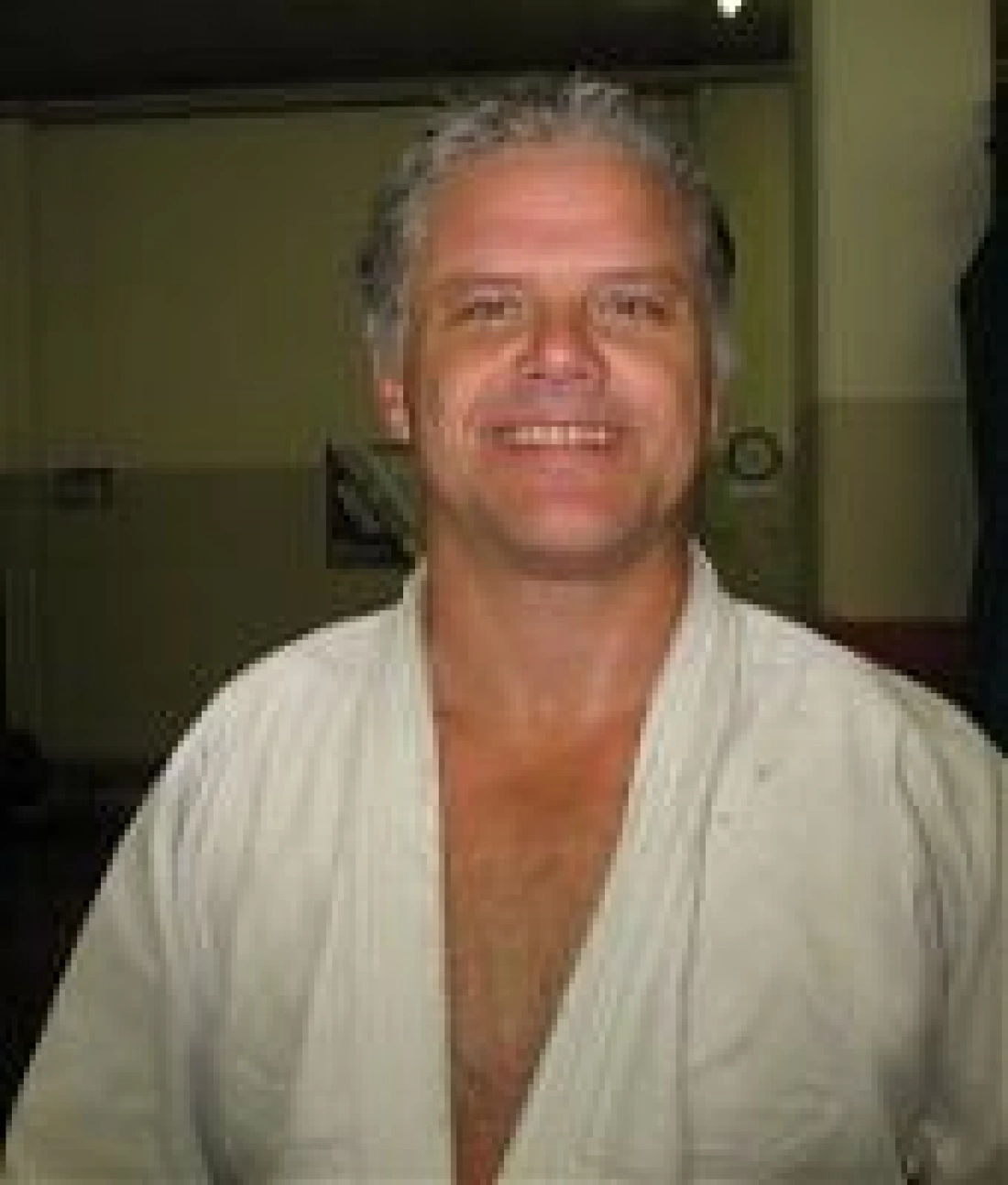 Mężczyzna w stroju do sztuk walki, uśmiechający się w pomieszczeniu treningowym.