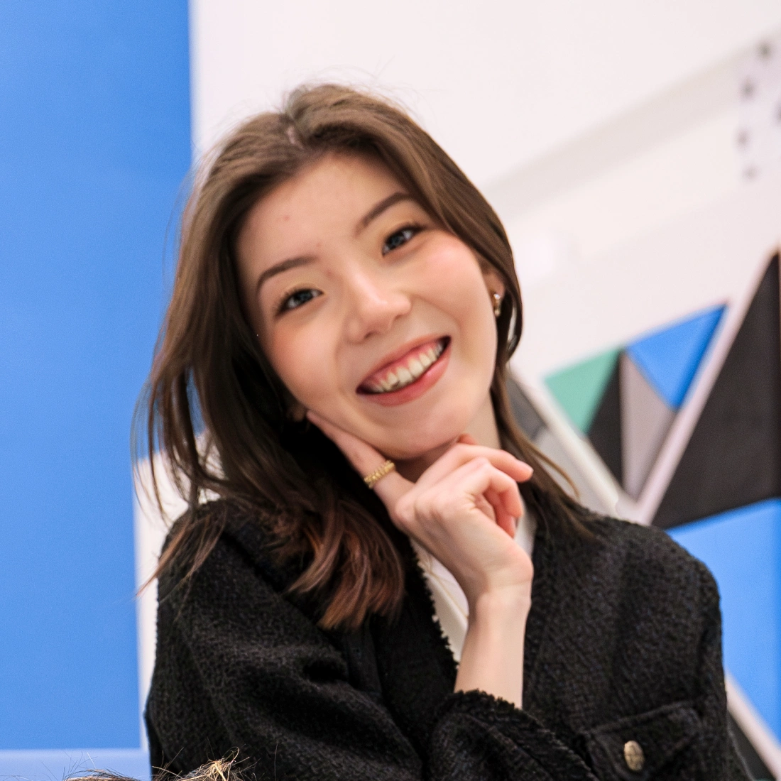 Uśmiechnięta kobieta z włosami w odcieniach brązu, stojąca na tle kolorowych ścian.