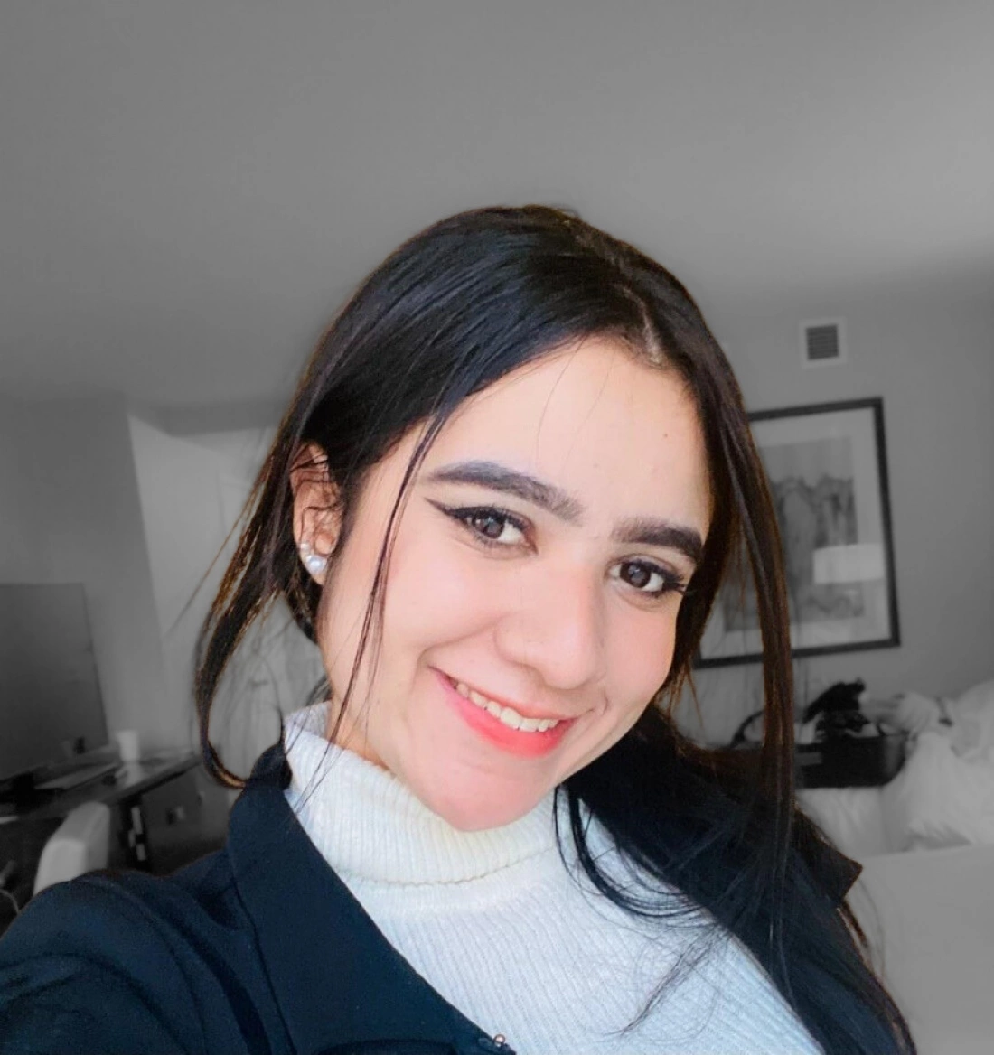 Młoda kobieta uśmiecha się, stojąc w jasnym pomieszczeniu.