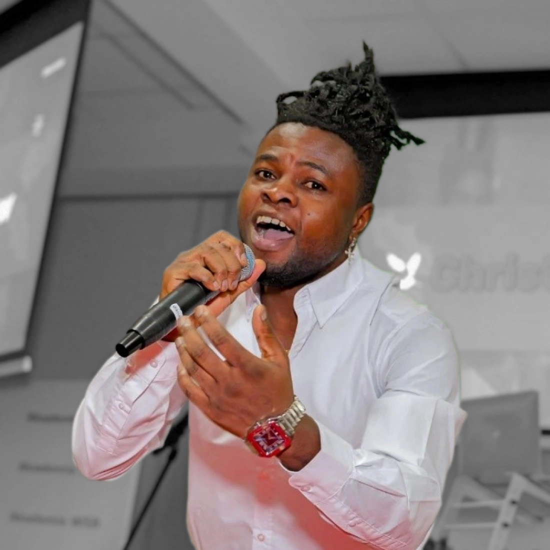 Mężczyzna w białej koszuli śpiewa do mikrofonu podczas wydarzenia.