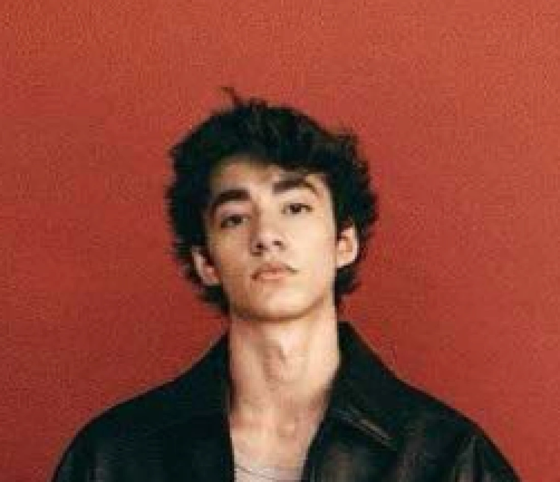 Młody mężczyzna w ciemnej kurtce na tle czerwonej ściany.