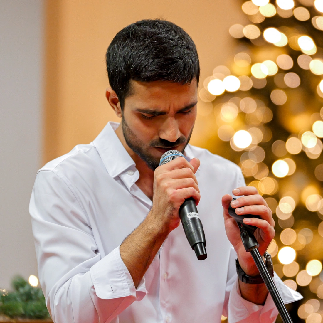 Mężczyzna śpiewa z mikrofonem, skupiony, w tle rozświetlone choinki.