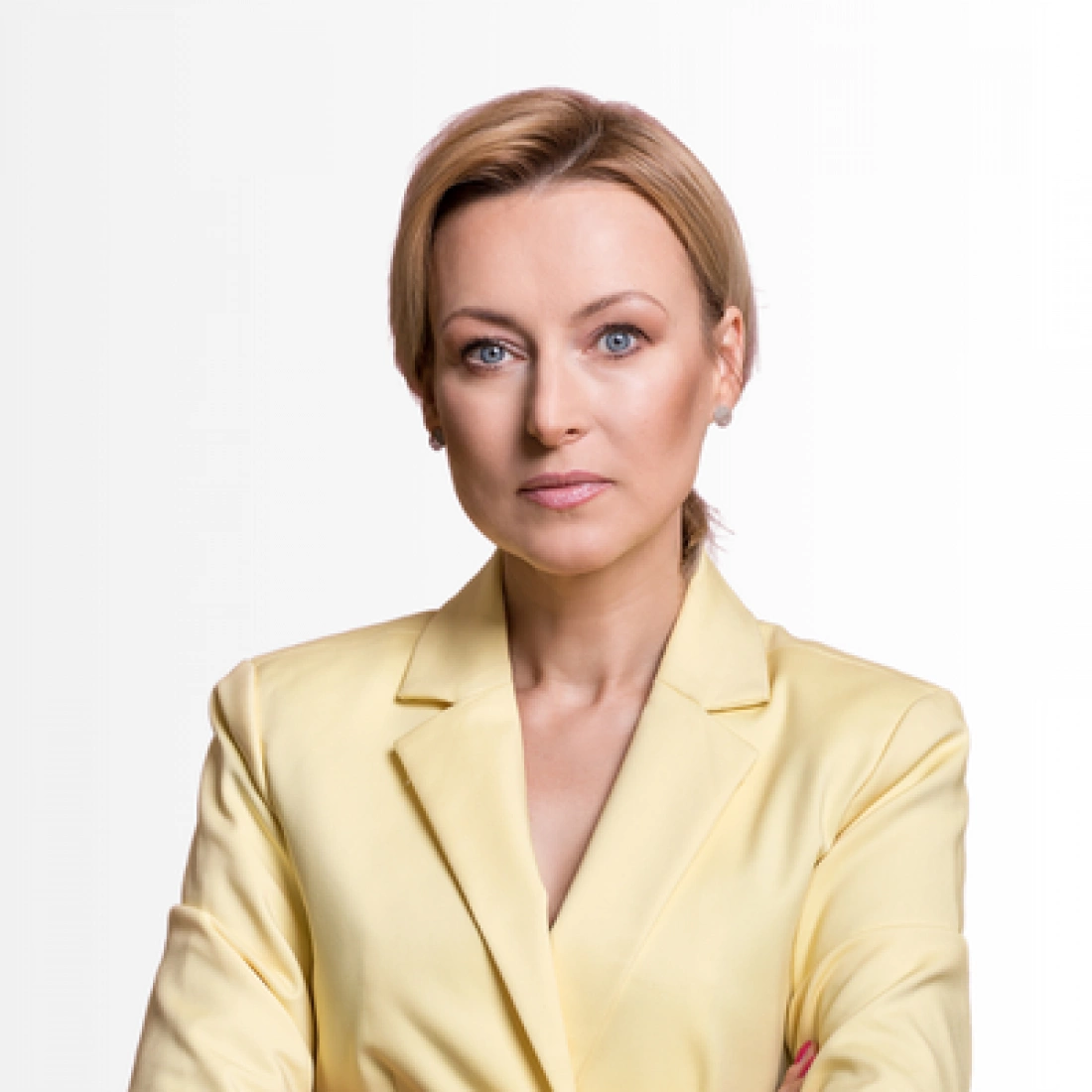 Kobieta w żółtej marynarce, z poważnym wyrazem twarzy, stoi na tle jasnego tła.
