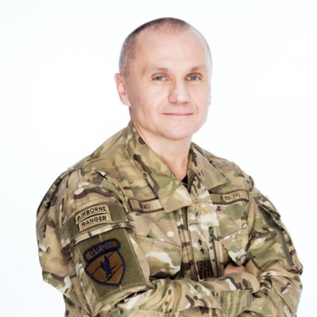 Mężczyzna w mundurze wojskowym z uśmiechem, ręce skrzyżowane na piersi.