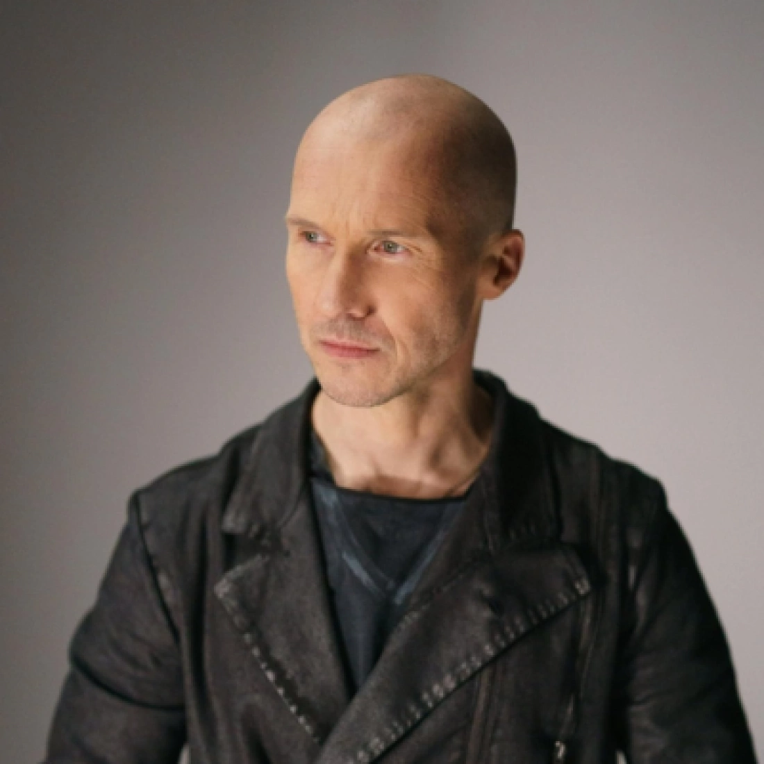 Mężczyzna w czarnej kurtce z zauważalnie łysą głową, patrzący w dal.