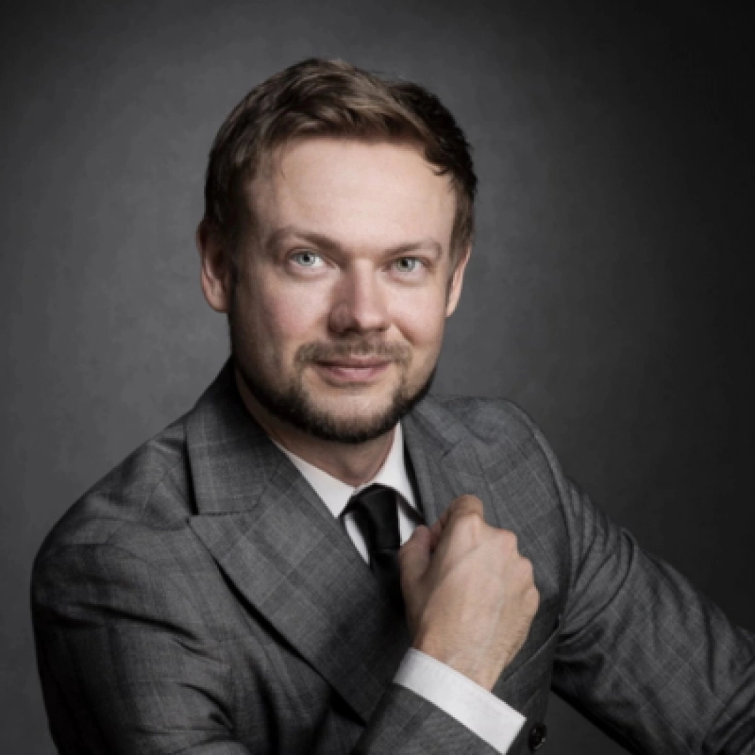 Mężczyzna w eleganckim garniturze z uśmiechem, pozujący w ciemnym tle.