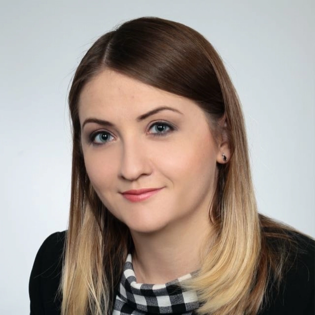 Portret młodej kobiety z blond włosami, uśmiechającej się lekko na neutralnym tle.